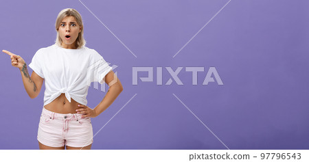Girl being unhappy with unfair thing happened. Shocked displeased complaining, confused woman with tanned skin blond hair and tattoos opening mouth and frowning from jealousy or regret pointing left Girl being unhappy with unfair thing happened. Shocked displeased complaining, confused woman with tanned skin blond hair and tattoos opening mouth and frowning from jealousy or regret pointing left 97796543