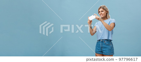 Girl trying to take photo of pet moving fast staring intense at smartphone screen pointing phone camera left feeling focused while taking picture on cellphone over blue background Girl trying to take photo of pet moving fast staring intense at smartphone screen pointing phone camera left feeling focused while taking picture on cellphone over blue background 97796617