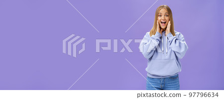 Woman joyfully smiling at camera and touching cheeks as if being surprised and happy see friend meeting person in airport feeling cheerful to reunite standing over purple background in cute hoodie Woman joyfully smiling at camera and touching cheeks as if being surprised and happy see friend meeting person in airport feeling cheerful to reunite standing over purple background in cute hoodie 97796634