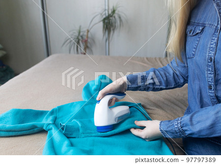 Machine for removing pellets. The girl uses a special device to remove lint from clothes. Restoration of old damaged clothes. Machine for removing pellets. The girl uses a special device to remove lint from clothes. Restoration of old damaged clothes. 97797389