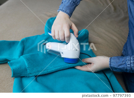 Machine for removing pellets. The girl uses a special device to remove lint from clothes. Restoration of old damaged clothes. 97797393