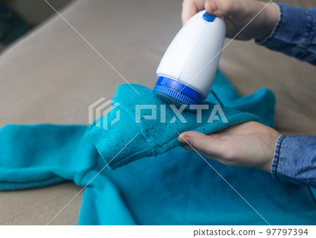 Machine for removing pellets. The girl uses a special device to remove lint from clothes. Restoration of old damaged clothes. 97797394
