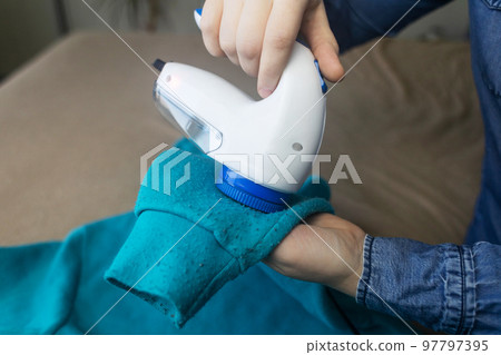 Machine for removing pellets. The girl uses a special device to remove lint from clothes. Restoration of old damaged clothes. 97797395
