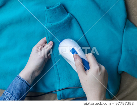 Machine for removing pellets. The girl uses a special device to remove lint from clothes. Restoration of old damaged clothes. Machine for removing pellets. The girl uses a special device to remove lint from clothes. Restoration of old damaged clothes. 97797398