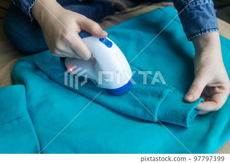 Machine for removing pellets. The girl uses a special device to remove lint from clothes. Restoration of old damaged clothes. Machine for removing pellets. The girl uses a special device to remove lint from clothes. Restoration of old damaged clothes. 97797399
