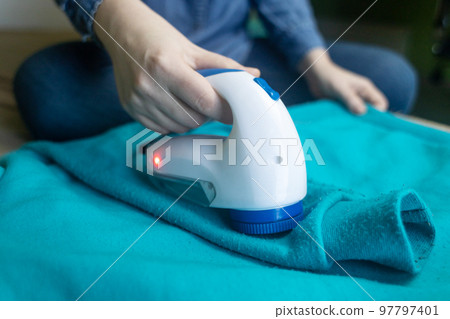 Machine for removing pellets. The girl uses a special device to remove lint from clothes. Restoration of old damaged clothes. Machine for removing pellets. The girl uses a special device to remove lint from clothes. Restoration of old damaged clothes. 97797401