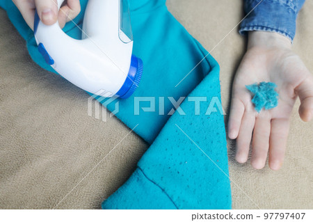 Machine for removing pellets. The girl uses a special device to remove lint from clothes. Restoration of old damaged clothes. 97797407