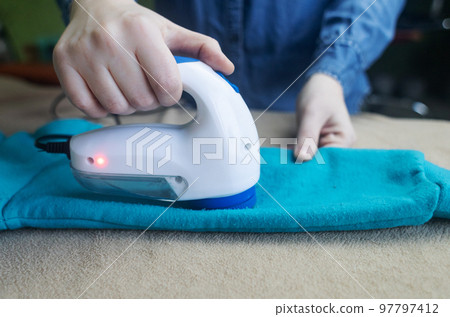 Machine for removing pellets. The girl uses a special device to remove lint from clothes. Restoration of old damaged clothes. 97797412