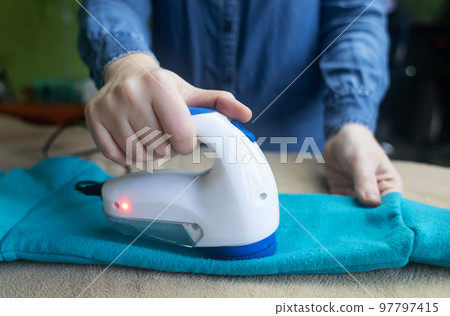 Machine for removing pellets. The girl uses a special device to remove lint from clothes. Restoration of old damaged clothes. Machine for removing pellets. The girl uses a special device to remove lint from clothes. Restoration of old damaged clothes. 97797415