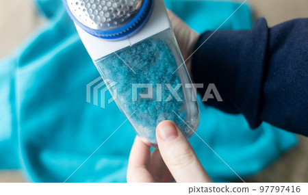 Machine for removing pellets. The girl uses a special device to remove lint from clothes. Restoration of old damaged clothes. Machine for removing pellets. The girl uses a special device to remove lint from clothes. Restoration of old damaged clothes. 97797416