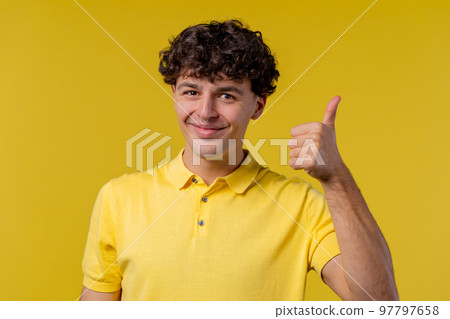 Positive curly man makes hand sign like, thumbs up gesture. Happy student guy in yellow, correct 97797658