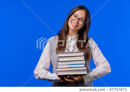 Asian clever student holds stack of university books from college library on blue background. Happy 97797671