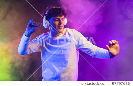 Positive man listening music with headphones, dancing on dark neon background. Stylish student guy Positive man listening music with headphones, dancing on dark neon background. Stylish student guy 97797686