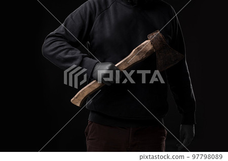A man in gloves holds an ax in his hands against a black background 97798089