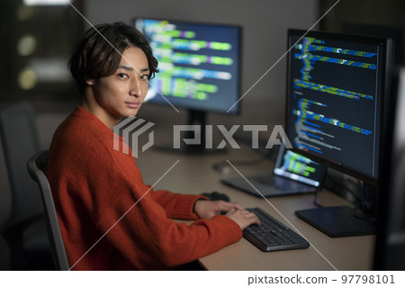 晚上辦公室一個年輕男子在電腦上工作看著相機肖像 晚上辦公室一個年輕男子在電腦上工作看著相機肖像 97798101