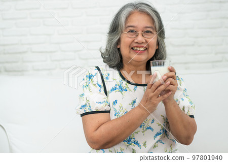 Asian Senior woman holding glass milk while relaxing on a sofa living room for retirement wellness. Elderly Woman drinking a glass of milk to maintain her wellbeing. Concept of wellness and healthy. Asian Senior woman holding glass milk while relaxing on a sofa living room for retirement wellness. Elderly Woman drinking a glass of milk to maintain her wellbeing. Concept of wellness and healthy. 97801940