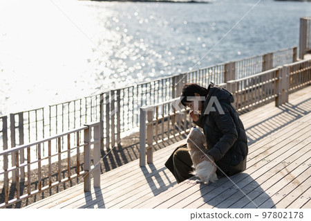 Owner woman relaxing with her dog on the terrace deck with the winter sea in the background Owner woman relaxing with her dog on the terrace deck with the winter sea in the background 97802178