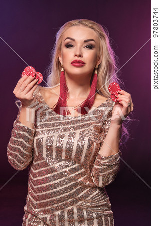 Blonde woman with a perfect hairstyle and bright make-up is posing with gambling chips in her hands. Casino, poker. Blonde woman with a perfect hairstyle and bright make-up is posing with gambling chips in her hands. Casino, poker. 97803744