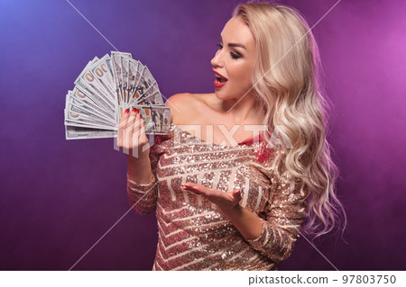 Blonde woman with a perfect hairstyle and bright make-up is posing with fan of hundred dollar bills in her hands. Casino, poker. Blonde woman with a perfect hairstyle and bright make-up is posing with fan of hundred dollar bills in her hands. Casino, poker. 97803750