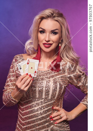 Blonde woman with a perfect hairstyle and bright make-up is posing with playing cards in her hands. Casino, poker. 97803767
