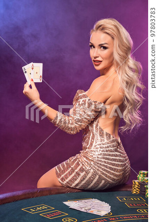 Blonde woman with a perfect hairstyle and bright make-up is posing with playing cards in her hands. Casino, poker. 97803783