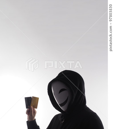 Hacker man and credit cards in hand. Represent credit cards personal data stolen by anonymous man in Black hood shirt. Credit cards data security and Cyber crime digital. Money transection unsecured. 97803830