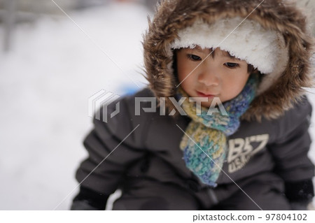 A boy wearing a down jacket and playing in the snow 97804102