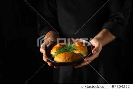 The baker holds in his hands a plate with freshly baked pies or pirozhki with dill. Free black space for menu or recipe. Ukrainian national cuisine The baker holds in his hands a plate with freshly baked pies or pirozhki with dill. Free black space for menu or recipe. Ukrainian national cuisine 97804252