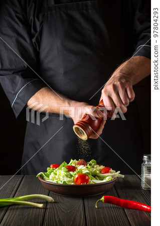 Chef adds peppers to a fresh vegetable salad in a restaurant kitchen. Close-up of cook hands holding a mill. Cooking healthy and tasty food Chef adds peppers to a fresh vegetable salad in a restaurant kitchen. Close-up of cook hands holding a mill. Cooking healthy and tasty food 97804293