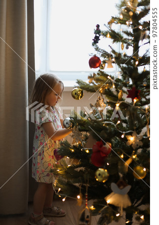 Little girl decorating christmas tree with toys and baubles. Cute kid preparing home for xmas celebration. Little girl decorating christmas tree with toys and baubles. Cute kid preparing home for xmas celebration. 97804555