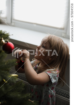 Little girl decorating christmas tree with toys and baubles. Cute kid preparing home for xmas celebration. 97804558