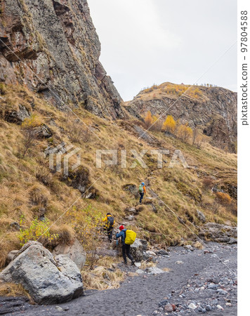 Autumn trekking on footpath alone Caucasus rocks. Group of tourists with backpacks climbs the mountains along the autumn trail. 97804588