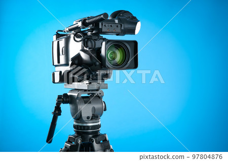 Modern professional video camera on blue background Modern professional video camera on blue background 97804876