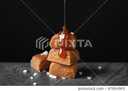 Pouring delicious salted caramel on candies against black background Pouring delicious salted caramel on candies against black background 97804963