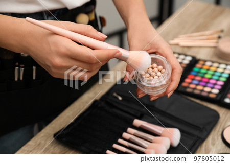 Professional makeup artist with brush and blusher at wooden table indoors, closeup Professional makeup artist with brush and blusher at wooden table indoors, closeup 97805012