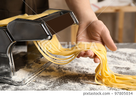 Woman preparing noodles with pasta maker machine at table indoors, closeup Woman preparing noodles with pasta maker machine at table indoors, closeup 97805034