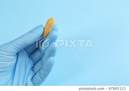 Closeup view of woman holding suppository on light blue background, space for text. Hemorrhoid treatment 97805121