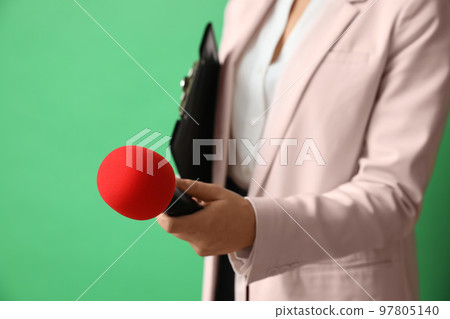 Journalist with microphone and clipboard on green background, closeup 97805140