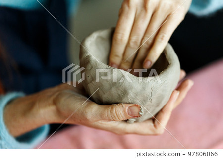 Women's hands knead the clay and sculpt a cup or bowl from it. The process of manufacturing a ceramic product,close up 97806066