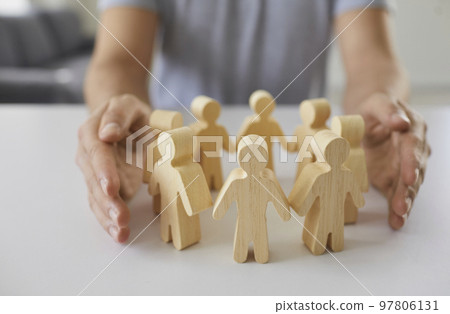 Man wraps two hands around wooden figurines of people standing in circle on table. Man wraps two hands around wooden figurines of people standing in circle on table. 97806131