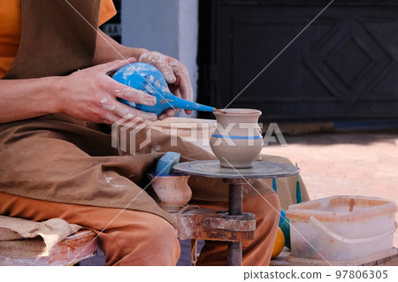 Potter uses a tool to cover clay pot with paint. Pottery and craftsmanship concept. 97806305
