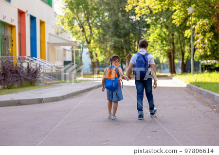 a little girl and a boy in a white shirt with backpacks go on the way to school. a little girl and a boy in a white shirt with backpacks go on the way to school. 97806614