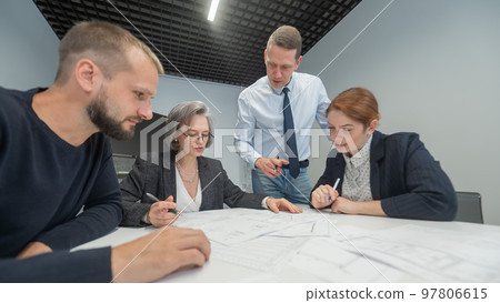 The boss gives instructions to three employees in the office conference room. Brainstorming engineers and architects. The boss gives instructions to three employees in the office conference room. Brainstorming engineers and architects. 97806615