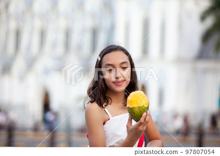 Beautiful tourist girl eating mango at the Ortiz Bridge with La Ermita church on background in the city of Cali in Colombia Beautiful tourist girl eating mango at the Ortiz Bridge with La Ermita church on background in the city of Cali in Colombia 97807054