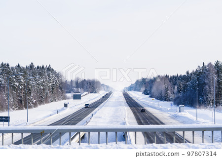 Winter highway. Asphalt road through a snowy forest. Car driving on a heavy winter road 97807314