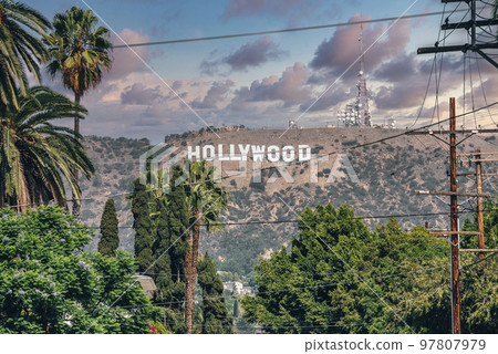 Los Angeles, USA. September 20, 2022. Distant view of Hollywood sign on beautiful Mount Lee seen through electricity pole and trees on sunny day with cloudy sky in background 97807979