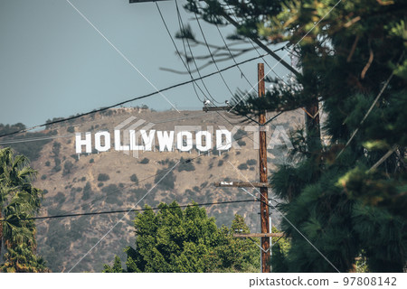 Los Angeles, USA. September 20, 2022. Distant view of Hollywood sign on beautiful Mount Lee seen through electricity pole and trees with sky in background during sunny day 97808142