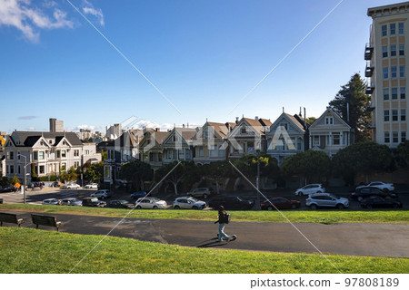 San Francisco, USA. September 20, 2022. Woman walking on hilly road with Painted Ladies Houses in a row under blue sky in the background at Alamo Square in California San Francisco, USA. September 20, 2022. Woman walking on hilly road with Painted Ladies Houses in a row under blue sky in the background at Alamo Square in California 97808189