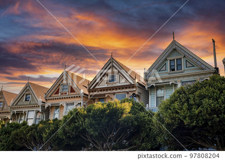 San Francisco, USA. September 20, 2022. Low angle view of historic victorian style houses and trees with orange cloudy sky in the background during sunset at Alamo Square in California San Francisco, USA. September 20, 2022. Low angle view of historic victorian style houses and trees with orange cloudy sky in the background during sunset at Alamo Square in California 97808204
