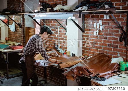 Asian craftsman in apron working with leather in workshop Asian craftsman in apron working with leather in workshop 97808530